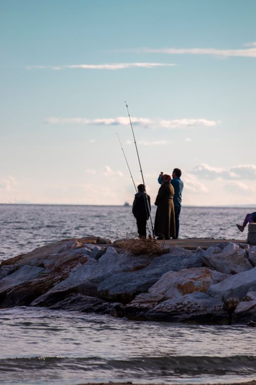 Free Family standing on rocks with fishing rods by the sea during sunset. Stock Photo