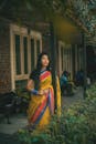 一位美丽的女子身着充满活力的传统黄色纱丽，站在郁郁葱葱的植物环绕的户外