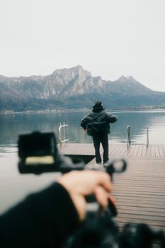 A person on a pier by a calm lake, surrounded by majestic mountains.