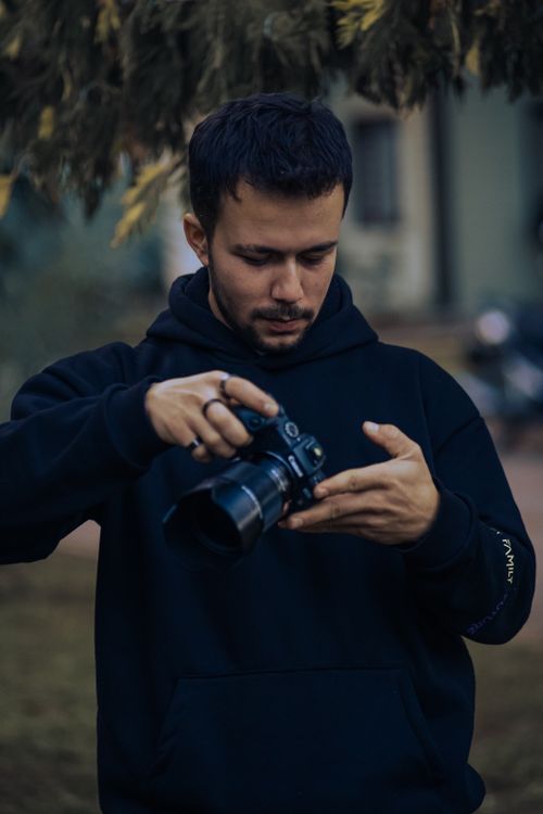 Free Young man in a dark hoodie checking camera settings in a natural outdoor setting. Stock Photo