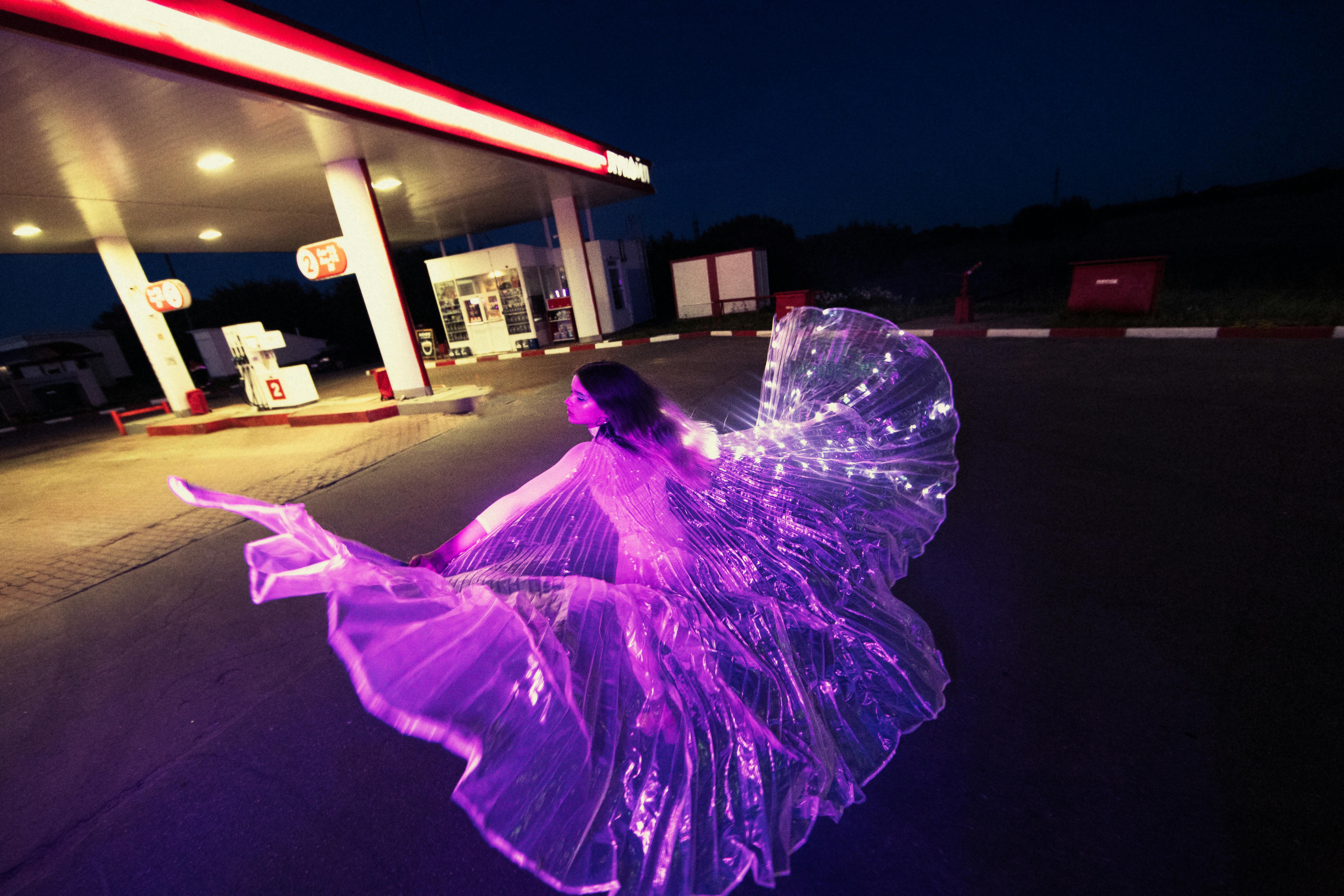 woman in glowing costume dancing at gas station at night