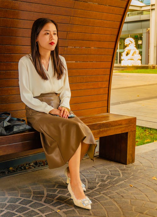 Model in a White Blouse and Brown Leather Skirt Sitting on a Bench