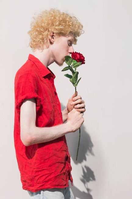 Stylish portrait of a man smelling a red rose, highlighting elegance and fashion.