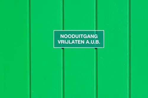 Emergency Exit Sign in Dutch Language Hanging on a Green Metal Wall