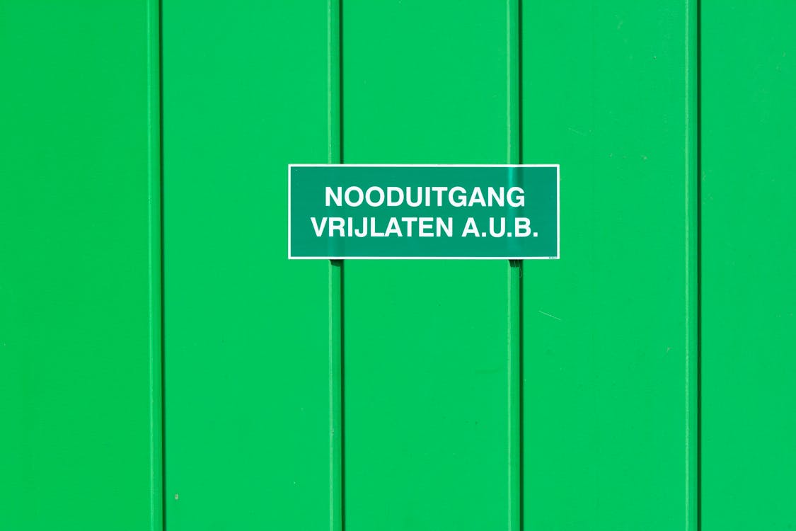 Emergency Exit Sign in Dutch Language Hanging on a Green Metal Wall