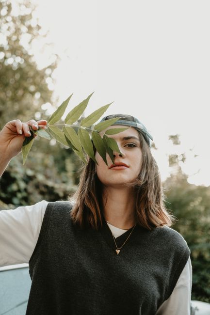 Portrait of a young woman holding a leaf in an outdoor setting, showcasing natural beauty and summer vibes.