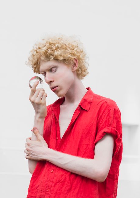 Stylish albino model in a red shirt holding a lensball, showcasing fashion and uniqueness.