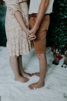 A couple stands barefoot in an indoor snow scene, holding hands, evoking winter romance.
