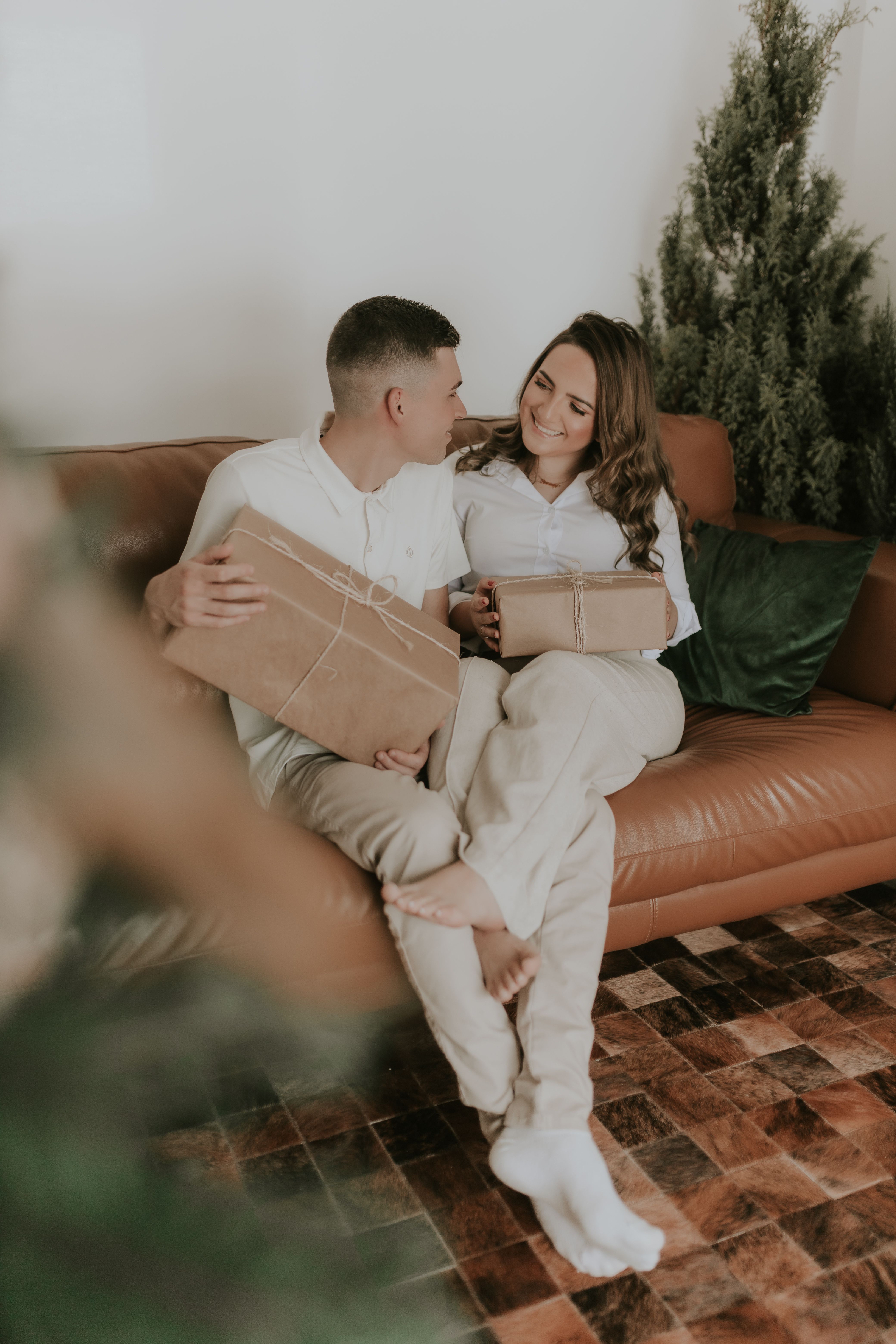 A joyful couple sitting on a sofa exchanging Christmas presents amidst festive decorations.