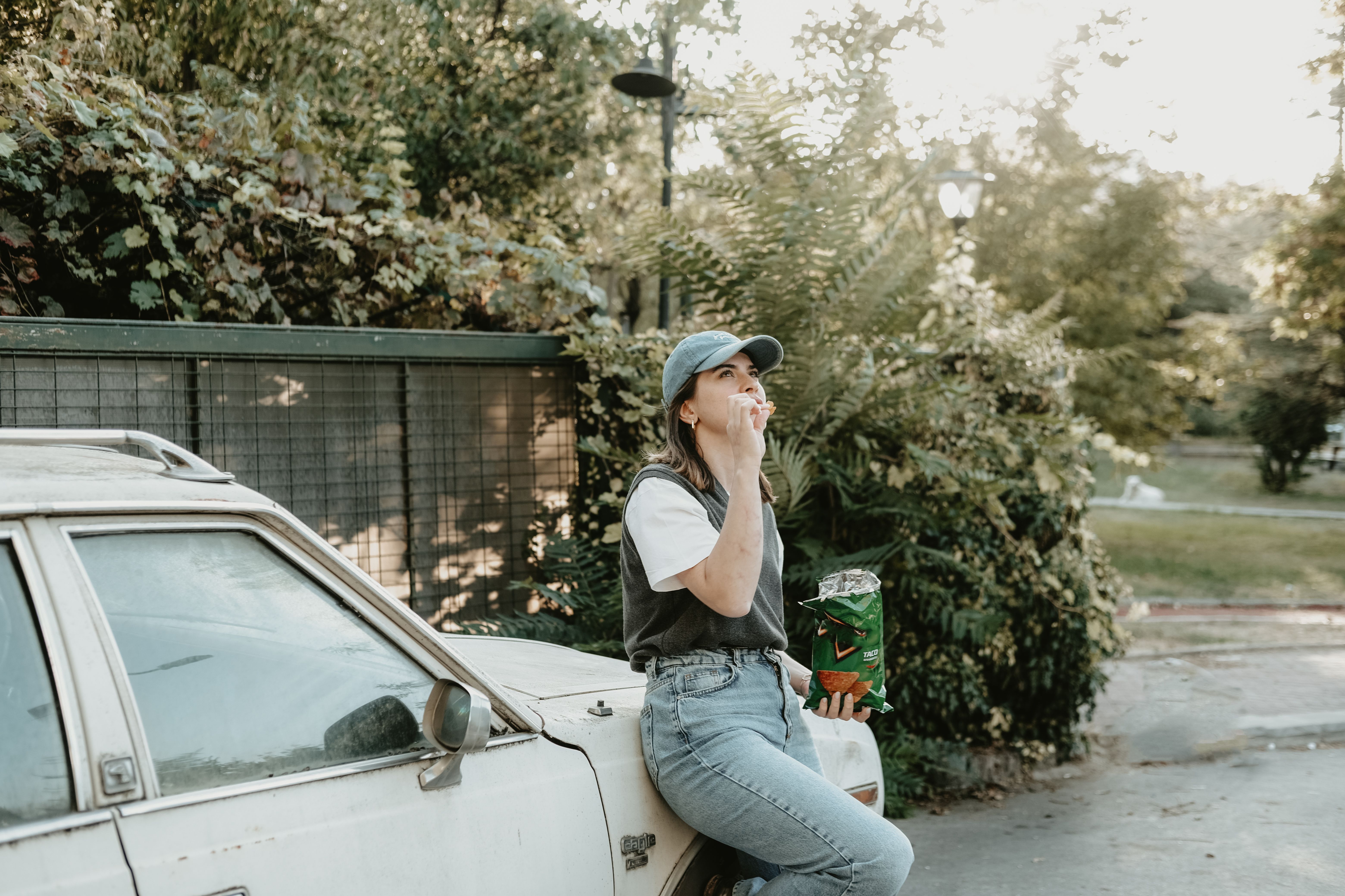 Jovem desfrutando de um momento de pausa ao ar livre, sentada sobre um carro, com o cenário de natureza ao fundo, refletindo um momento de descontração e convivência com o ambiente externo.