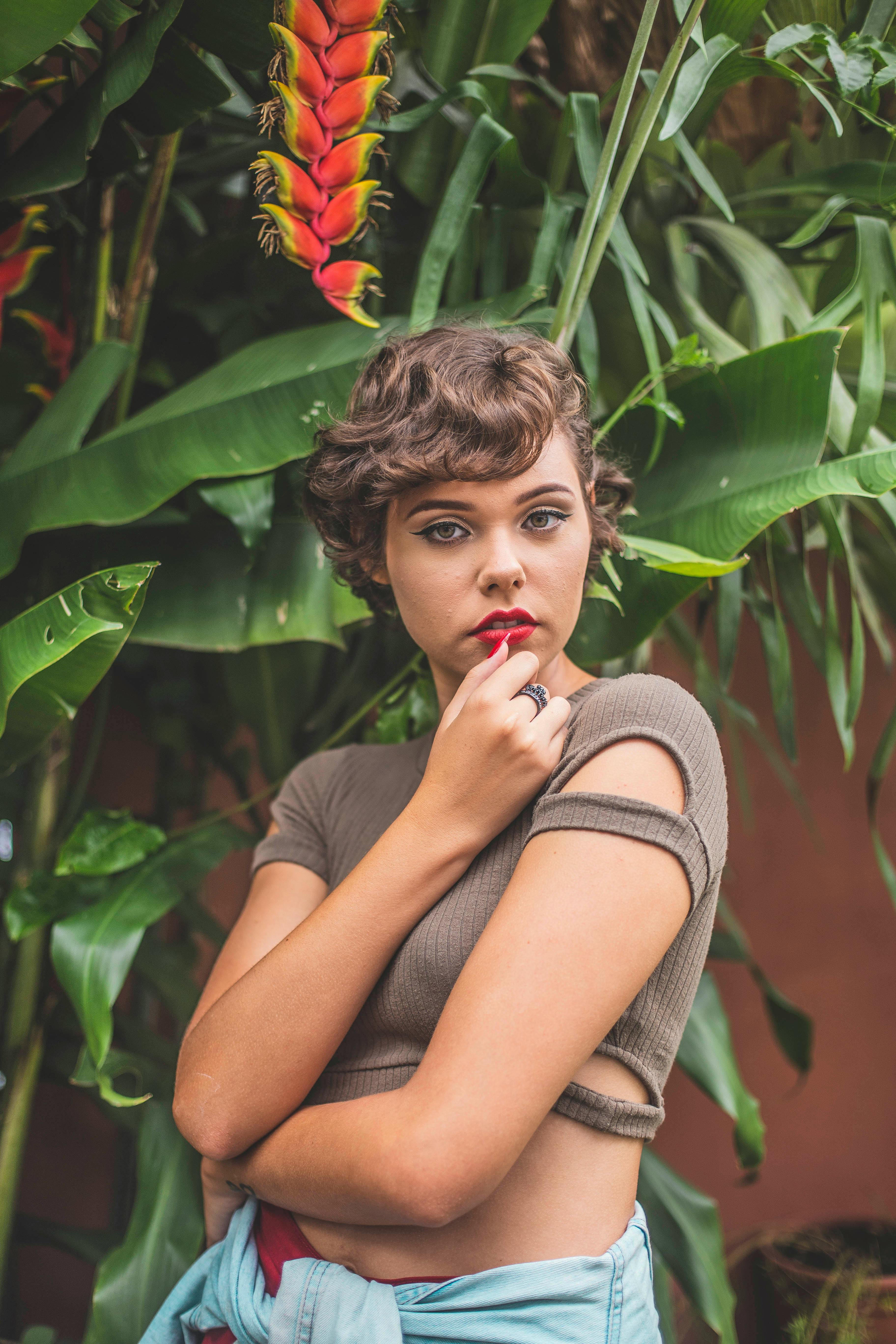 一位时尚的年轻女子在郁郁葱葱的热带树叶间摆姿，自然流露出美丽与自信