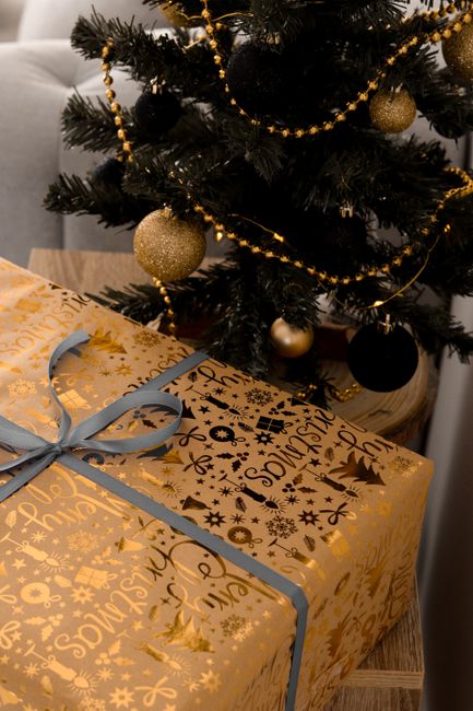 Beautiful Christmas gift with golden wrapping and ribbon under a decorated tree, perfect for holiday themes.