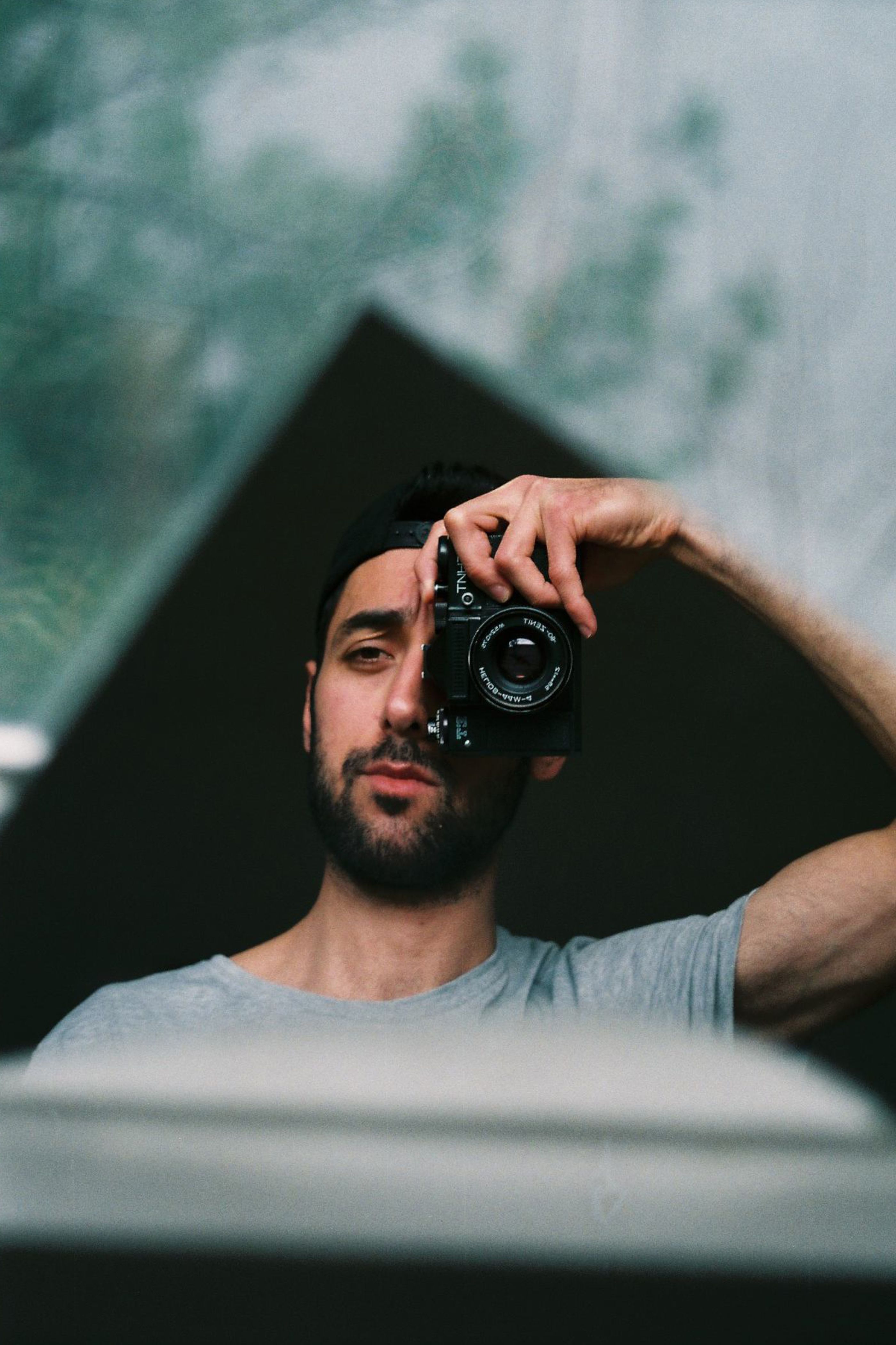 A man using a vintage camera in front of a mirror, capturing his reflection.