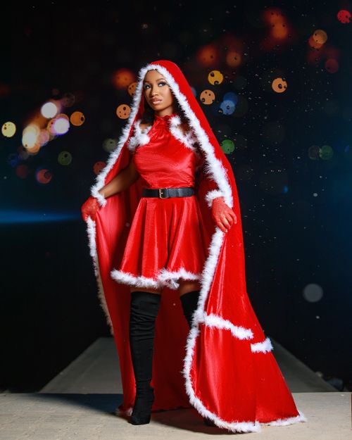 Free A woman poses in a red Santa costume with festive lights in the background. Stock Photo