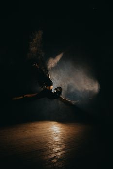 Silhouetted dancer leaping amidst smoke on a dark stage, exuding a powerful performance.