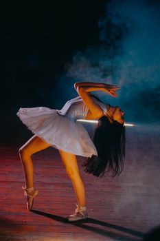 Elegant ballerina in white tutu performing on a dimly lit stage with dramatic lighting.
