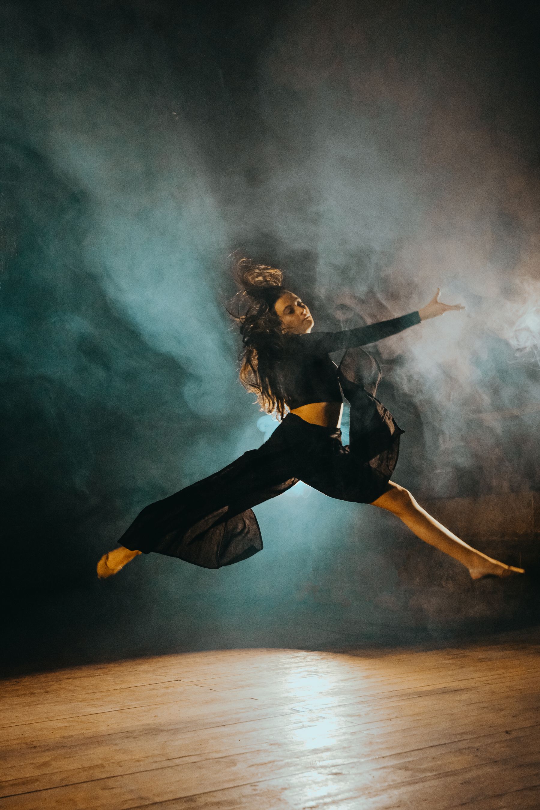 Bailarina saltando en el aire entre humo, sobre un escenario de madera