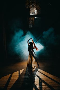 A mesmerizing silhouette of a dancer posing with colorful smoke on a stage.