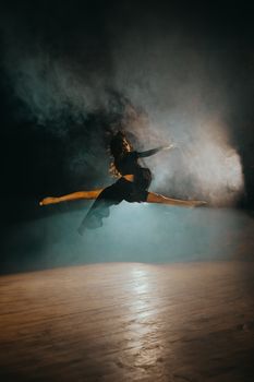 Graceful dancer performs a midair split on a misty stage with dramatic lighting.