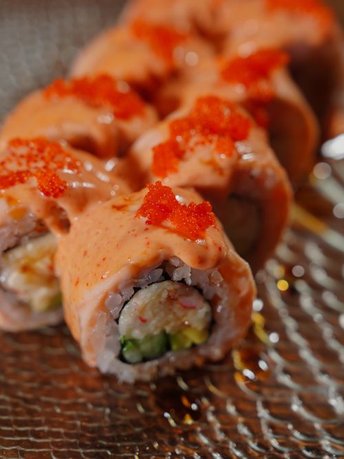 Free Close-up of sushi rolls topped with spicy mayo and fish roe, served on a textured glass plate. Stock Photo