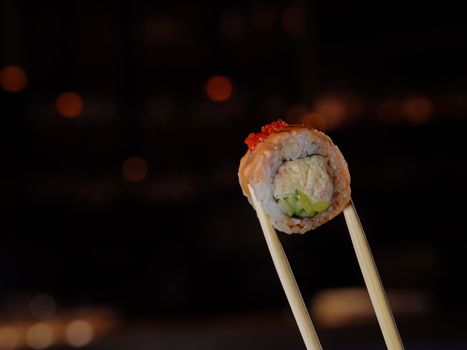 Delicious sushi roll held by chopsticks in a dark restaurant setting.