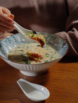 Close-up of a person holding a spoon with delicious soup in a ceramic bowl, creating a cozy dining ambiance.