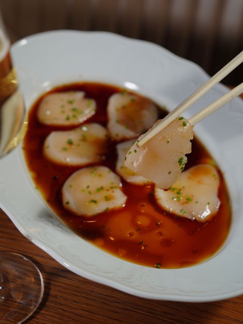 Free A close-up view of scallops in soy sauce, captured with chopsticks holding a piece. Stock Photo