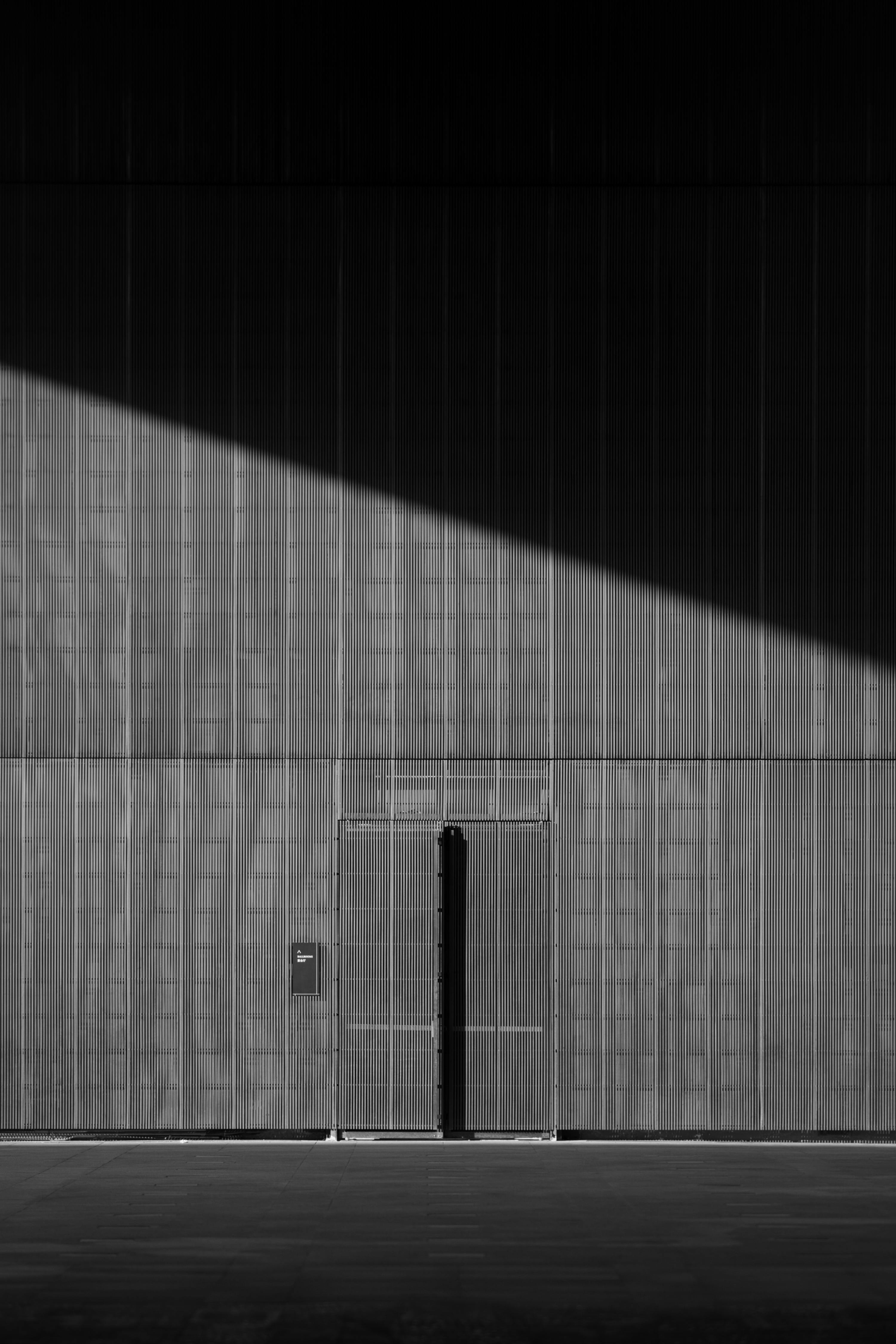 A modern, sunlit facade with a partly open door casting shadows, in black and white.