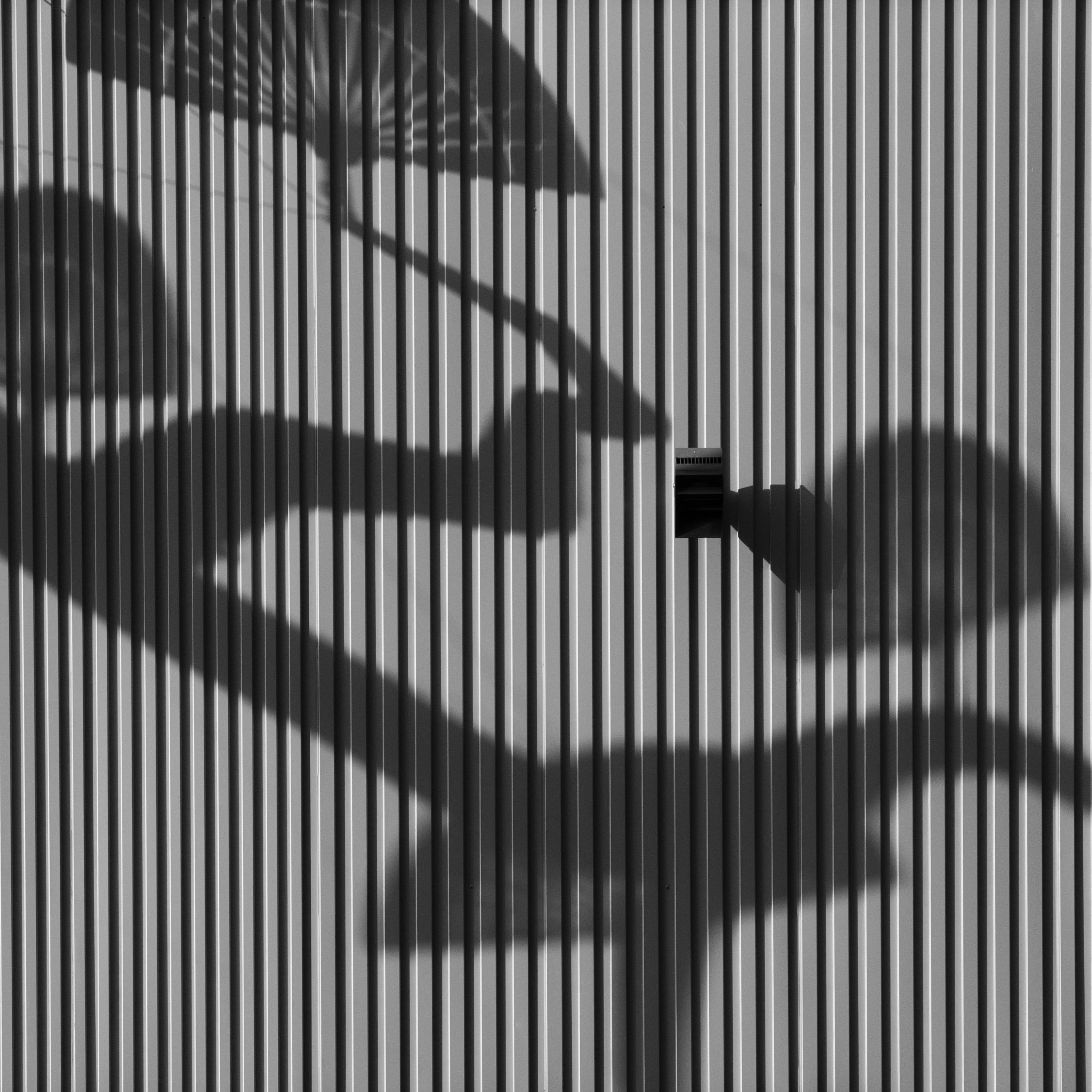 Shadows of objects casting on a textured corrugated metal wall in black and white.