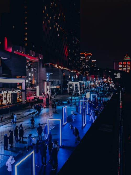 People Walking on an Illuminated Sidewalk in City at Night 
