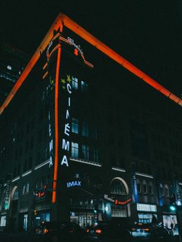 Night view of a neon-lit cinema facade in a bustling city with dramatic lighting.