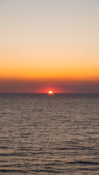 Peaceful sunset view with vibrant colors casting over a calm sea and wavy water surface.