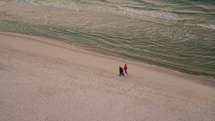 Parents Walking With Child On Beach