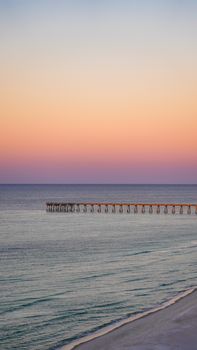 Tranquil scene of a long pier extending into the calm sea under a vivid sunset sky.