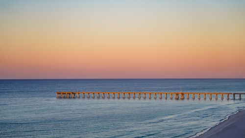 Free A tranquil beach scene featuring a pier extending into the calm sea under a colorful sunset sky. Stock Photo