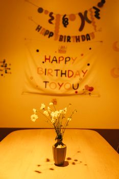 Warmly lit table scene with a birthday banner and floral arrangement in a vase.
