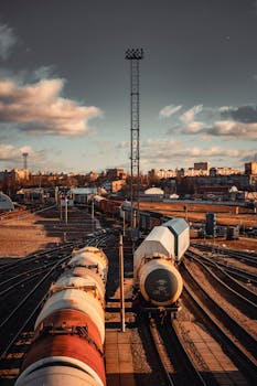Train yard with multiple railroad tracks and industrial cityscape under blue sky.