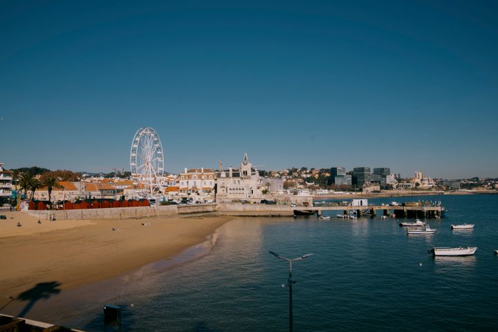 Pemandangan udara menakjubkan Cascais dengan pantai, kincir ria, dan bangunan bersejarah di tepi laut.