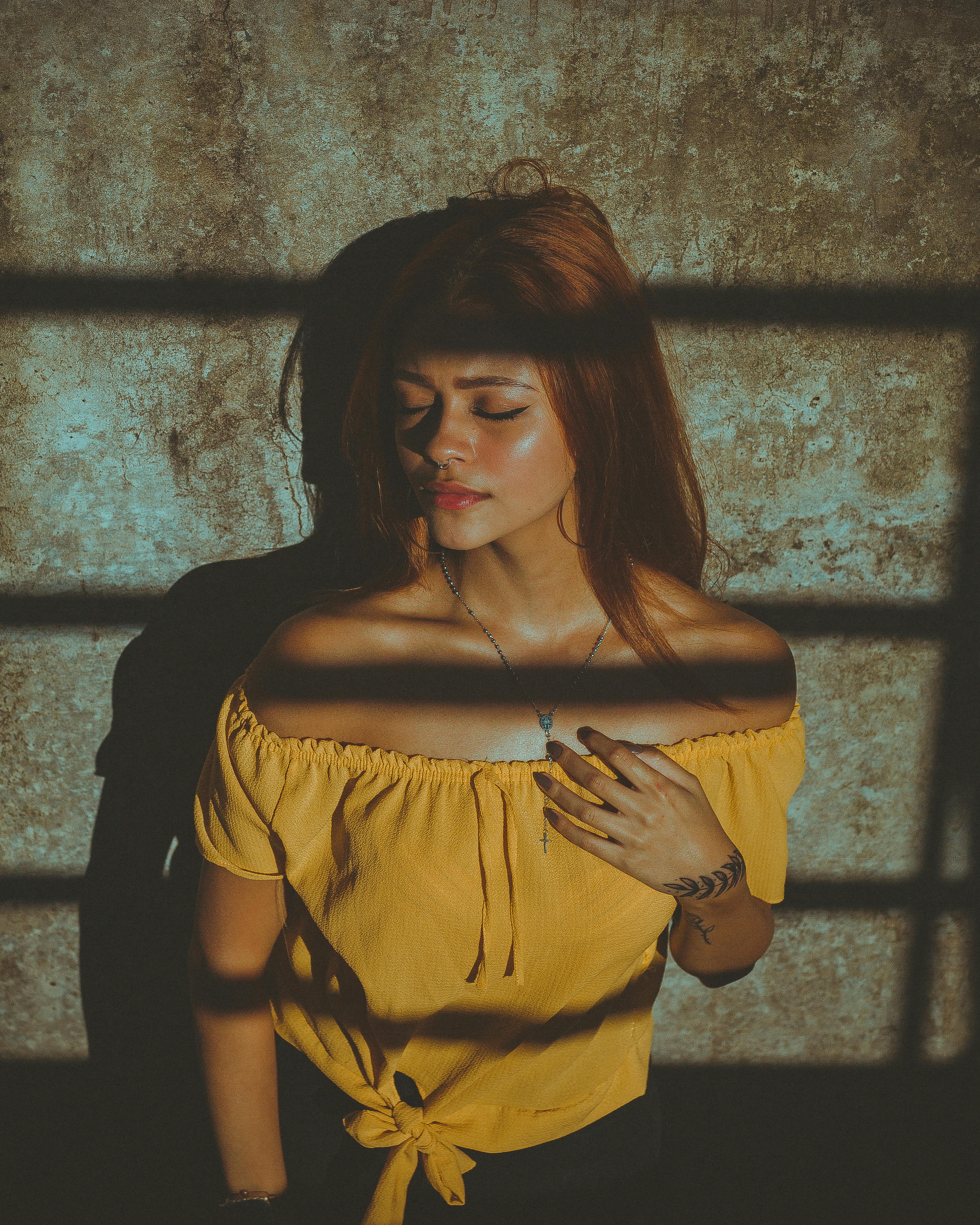 一幅艺术肖像，描绘了一位身穿黄色衬衫、闭着眼睛、沐浴在戏剧性光影中的女人