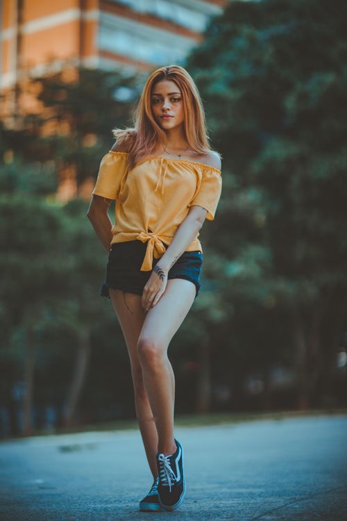 Free Fashionable woman in yellow blouse and shorts posing on a street with blurred background. Stock Photo