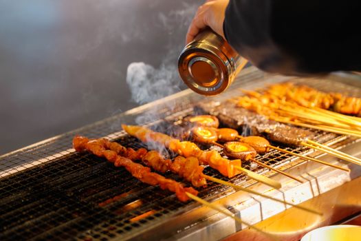 Close-up of skewers being seasoned on a grill. Perfect for barbecue lovers.