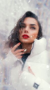 Striking portrait of a woman in winter attire, featuring bold red lipstick amidst falling snow, exuding elegance.