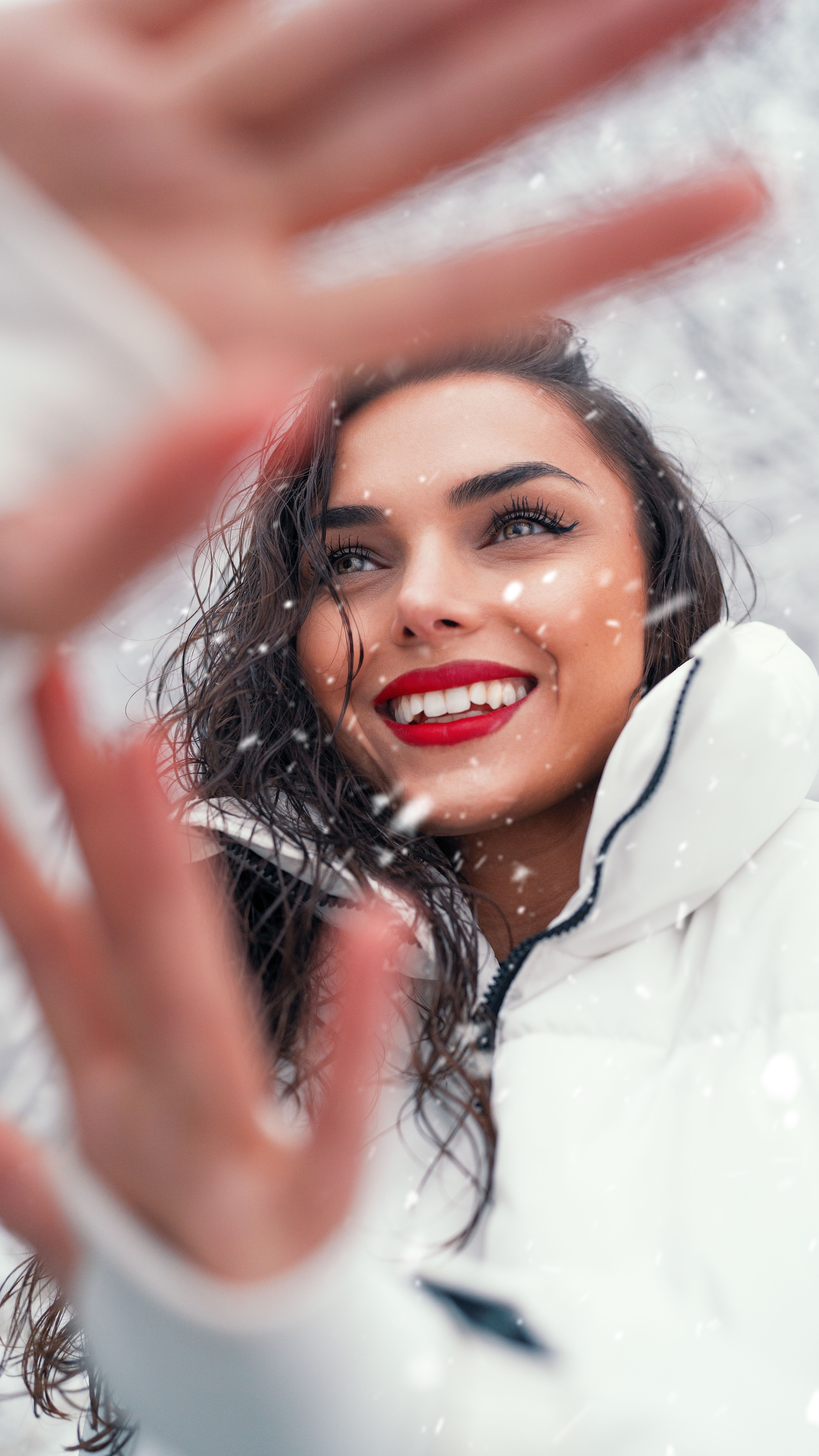 Smiling brunette woman enjoying the snow in a cozy white jacket, exuding warmth and joy.