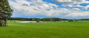 Serene Czech landscape featuring lush fields, a tranquil lake, and dense forest under a vast sky.