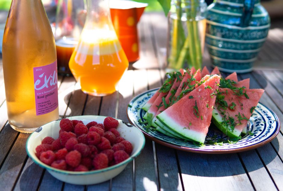 A tall glass of bright pink watermelon mint juice over ice, garnished with a mint sprig and a lime wedge, with fresh watermelon cubes in the background.
