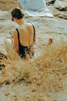 Back view of a woman sitting on a rocky beach in Helsinki, enjoying a summer day.