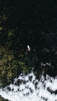 Drone shot of a canoe on the sea near the coast with visible waves, taken in Pilar, Philippines.
