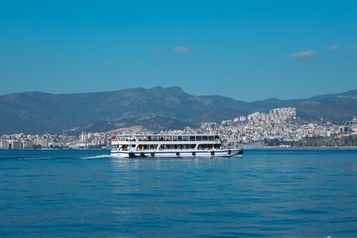 Free Ferry sailing on a clear day with İzmir cityscape and mountains in the background. Stock Photo
