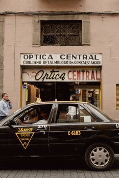Black taxi passing by an optical store in Puebla, capturing urban life vibe.