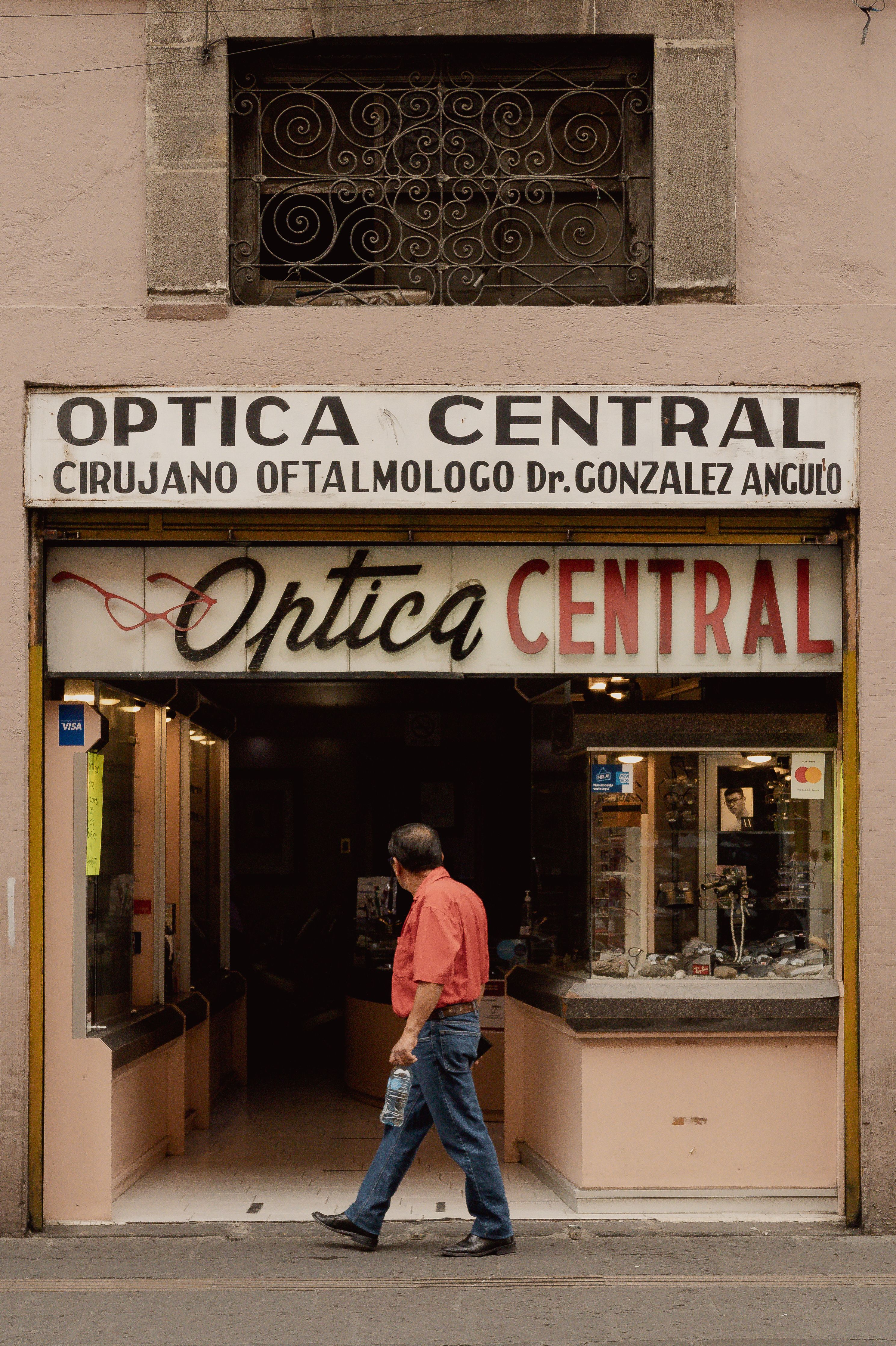 Man walking by Optica Central, an eyewear store in Heroica Puebla de Zaragoza, Mexico.
